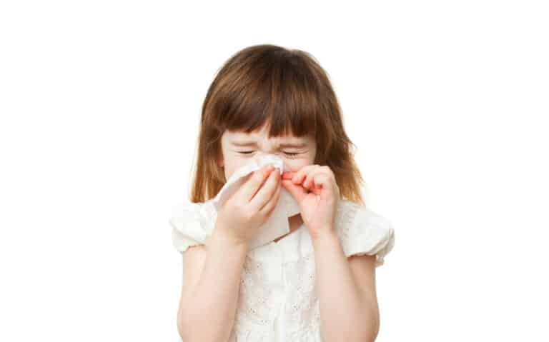 little girl sneezing into tissue